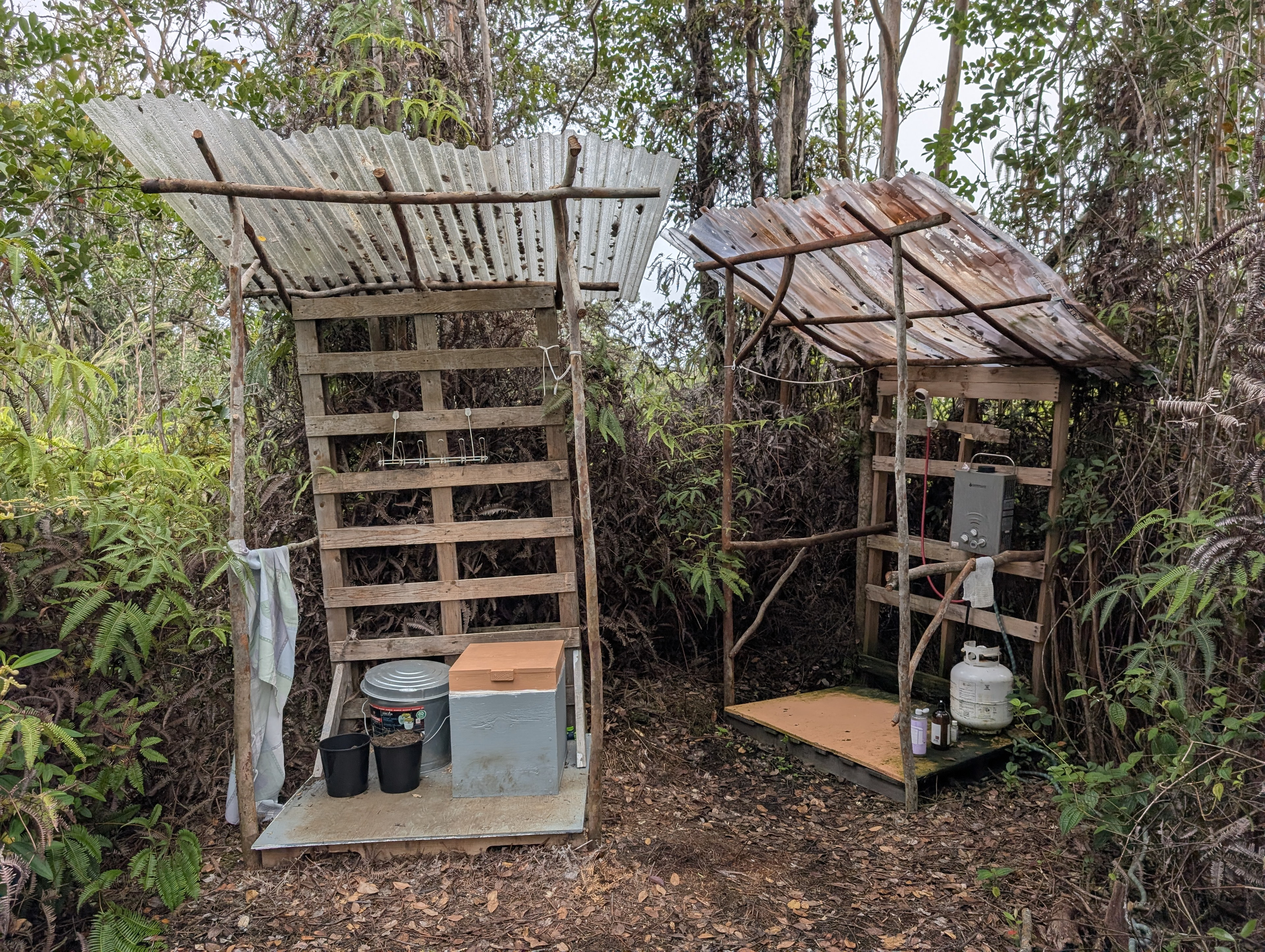 Composting toilet stall and jungle shower under corrugated roofs